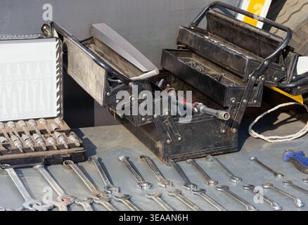 open black multi-tier cantilever toolbox sits on a metal workbench surrounded by an organized arrangement of silver steel wrenches and a socket set. Stock Photo