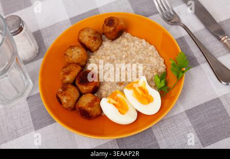 Soft-boiled eggs, golden meatballs and oatmeal on orange plate Stock Photo