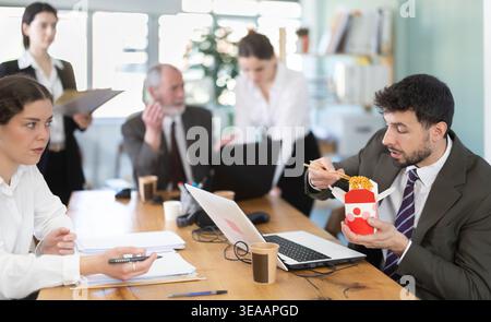 Man eats in office and spreads unpleasant smell of food, outraged colleagues scolding Stock Photo