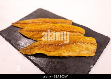 Three pieces of fish fillets are arranged neatly on a black slate tray. The setting is a food market in the afternoon, showcasing fresh seafood. Stock Photo