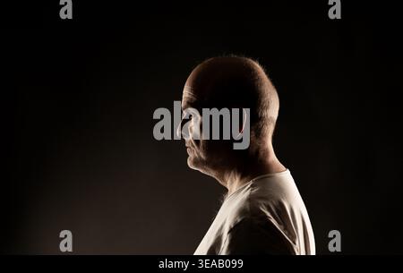 Mature man in profile with dramatic lighting on a dark background Stock Photo
