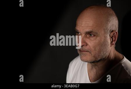 Middle aged man looking away, reflecting with a serious expression and dramatic lighting Stock Photo