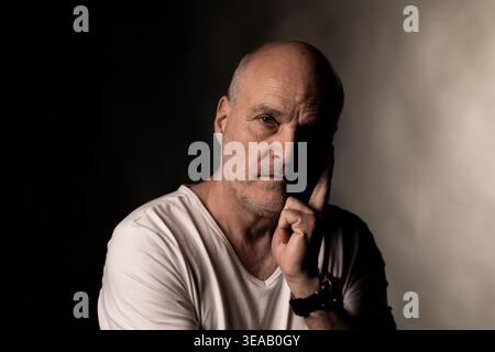 Serious bald man reflecting, thinking deeply against a dark background Stock Photo