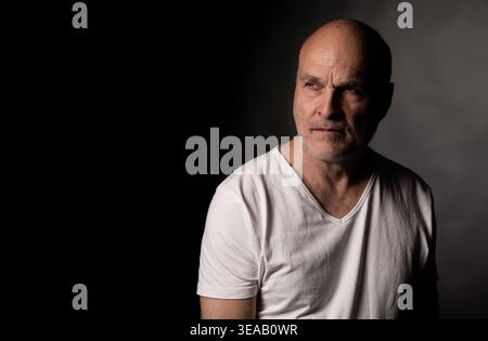 Bald man contemplating, thinking, or remembering on a dark background Stock Photo