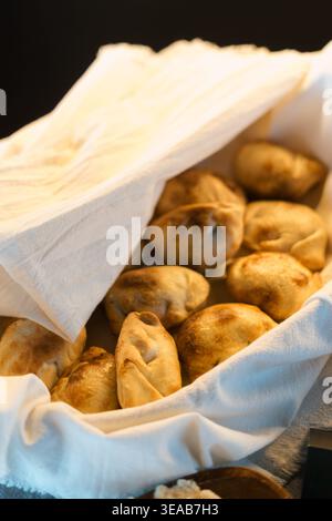 Golden-brown bread rolls rest in a white cloth-lined basket. Warm lighting highlights their crispy crusts. Paper towel folds gently over the top. Clos Stock Photo