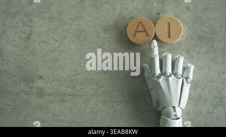 A white robotic hand points toward circular wooden blocks spelling the word AI on a stone background. Stock Photo