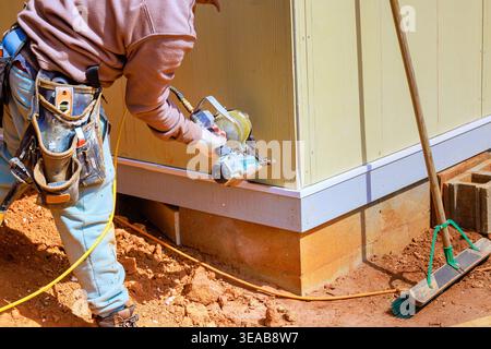 Worker using nail gun to attach panels on building site to materials to foundation Stock Photo