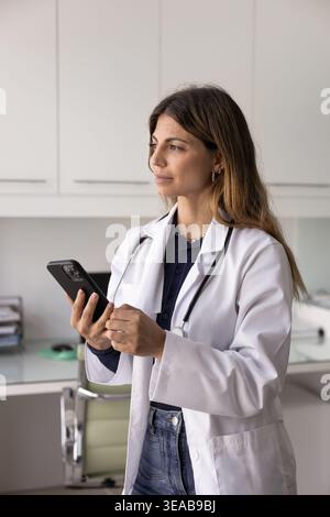 Young Latina woman, healthcare professional holding smartphone in workplace Stock Photo