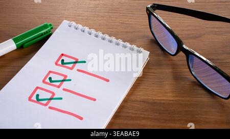 A hand drawn checklist with green check marks in red boxes on a white notepad with a marker and glasses nearby. Stock Photo