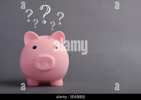 Piggy bank with question marks above on grey background, symbolizing financial uncertainty, decision making, and savings confusion. Stock Photo
