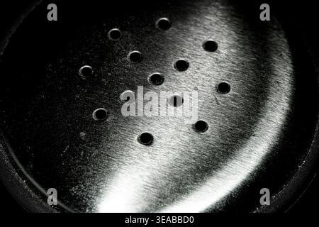 Macro closeup of stainless steel perforated surface with circular holes and brushed metal texture in dramatic lighting Stock Photo