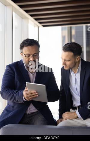 Two businessmen reviewing information on digital tablet during workday Stock Photo