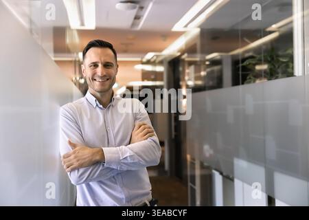 Portrait of businessman standing with arms crossed in office corridor Stock Photo