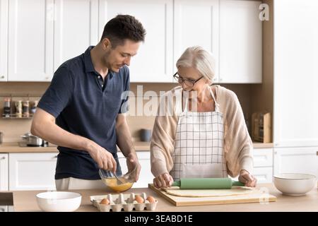 Older woman and young adult son cooking together Stock Photo