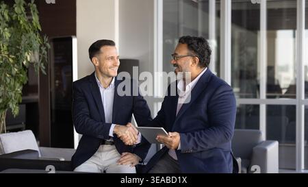 Two businessmen expressing respect, shaking hands during workday in office Stock Photo
