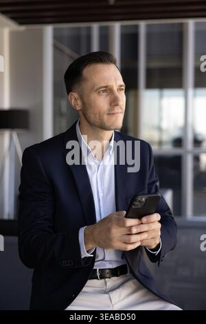 Thoughtful business man holding smartphone in office Stock Photo