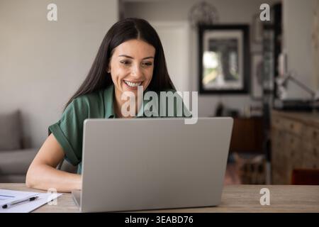 Smiling woman working on laptop at home office Stock Photo