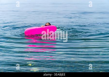 Woman swimming inflatable float enjoys a fun day splashing in the clear blue ocean during a bright sunny summer holiday Stock Photo