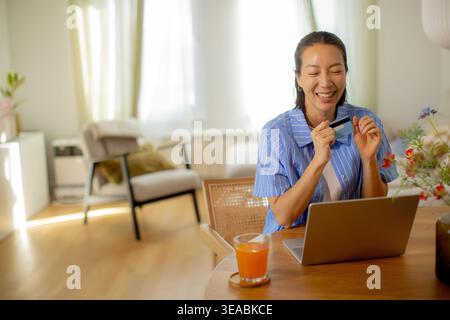 A joyful woman engages in a video call from her cozy home office, surrounded by natural light and cheerful decor. Stock Photo