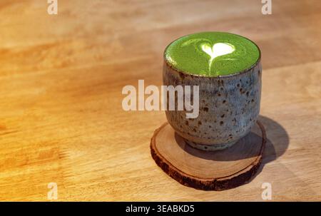Top view of hot matcha green tea latte with heart art in ceramic cup on wooden table. Japanese zen cafe concept with ample copy space. Stock Photo