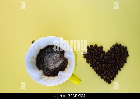 Top view after pouring hot water in yellow V60 dripper. Coffee dripping process on bright yellow background with heart shape beans. Stock Photo