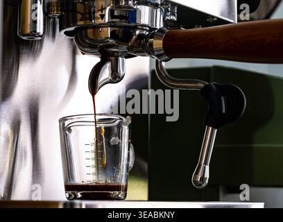 Close-up of espresso extraction from professional coffee machine. Stainless steel portafilter with wooden handle in specialty cafe. Stock Photo