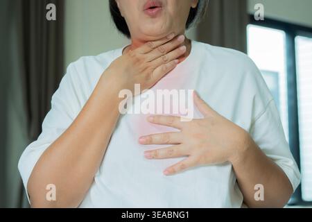 Woman suffering from Acid Reflux Or Heartburn standing in livingroom at home. Mature woman suffering from sore. Stock Photo