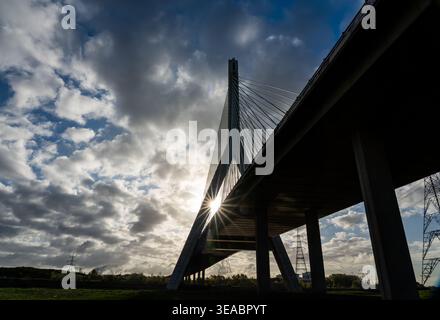 Flintshire Bridge cable-stayed pylon and sunstar silhouetted against dramatic cloudy sky with electricity pylons beyond Stock Photo