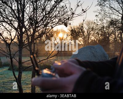 Drone pilot holding a remote control in a misty landscape at golden hour. Sunset background with glowing lens flare. Stock Photo