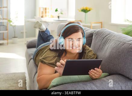 Chubby overweight young woman enjoys lazy day, lying on comfortable sofa Stock Photo