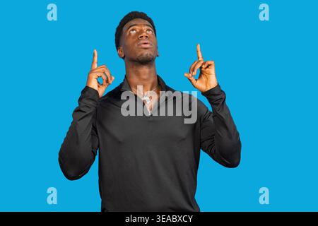 Young black man pointing fingers up with both hands on a blue background Stock Photo
