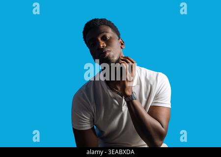 Young african man posing confidently in a studio, touching his neck Stock Photo