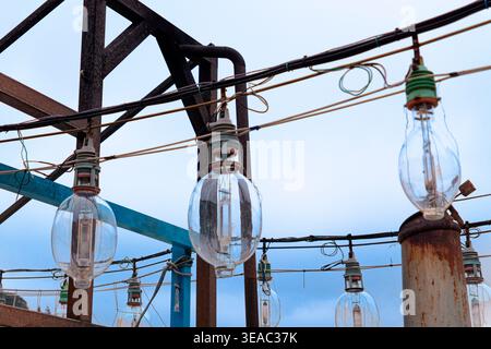 Close-up of large traditional glass fishing lamps hanging from rusted metal framework on a fishing vessel, with wires and blue sky backdrop in Taiwan. Stock Photo
