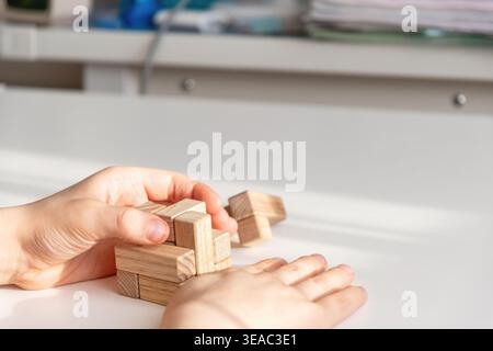 Child's hands solving a wooden brain teaser puzzle on a white table. Focus on logic, STEM education, and fine motor skills development Stock Photo