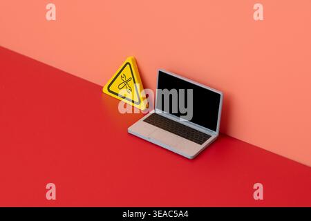 A miniature laptop next to a warning sign displaying a wrench and screwdriver icon. Minimalist concept representing IT support, computer repair Stock Photo