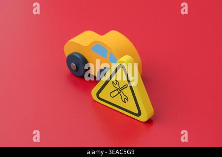 A yellow car on a red background with a sign displaying a wrench and screwdriver icon. A minimalist concept for car repair, service, and maintenance. Stock Photo