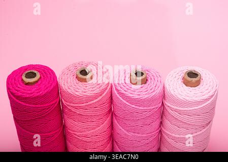 A set of four spools of handmade thread in various shades of pink, arranged on a matching pink background. Stock Photo