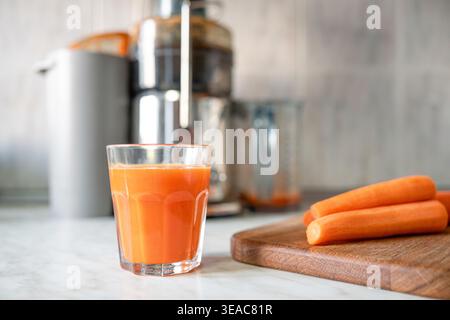 Carrot juice with fresh carrots on wooden cutting board with celery and apples, healthy eating, detox nutrition, natural ingredients for homemade juic Stock Photo