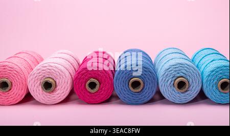 Several yarn spools in various pastel colors arranged in a row on a soft pink background. Stock Photo