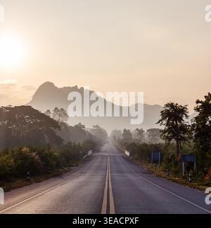 Highway in Northeast Thailand. Misty mountains in the background. Early morning light on the road. Trees lining the scenic route. Stock Photo