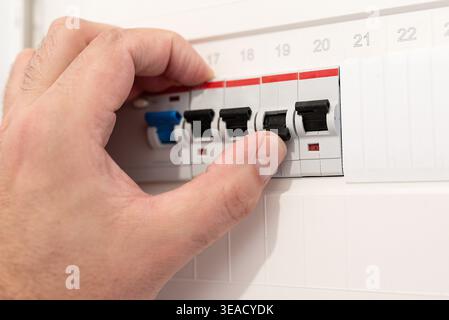 close-up of hand interacting with an electrical circuit breaker panel in German home. Person flips switch of fuse after electrical short. Maintenance Stock Photo