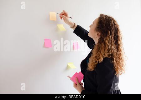 businesswoman using sticky notes on wall to writing strategy business plan to development Stock Photo