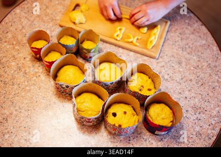 Hands preparing risen sweet bread dough with raisins in decorative paper molds on a kitchen countertop. Stock Photo