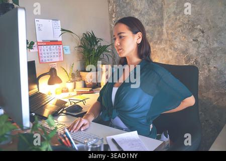 Typing, computer or woman with back pain in home office for bad posture, editing draft or remote work. PC, freelancer and journalist with sore spine Stock Photo