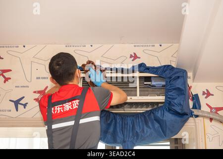 ZHONGSHAN China-April 19 2026: A JD Home Services technician is carefully wiping down a wall-mounted air conditioner. Stock Photo