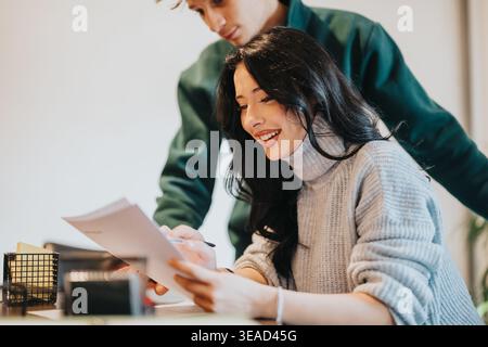 Two students studying together at a desk smiling while reviewing documents and collaborating Stock Photo