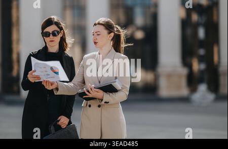 Two businesswomen reviewing charts and documents during an outdoor meeting in an urban setting Stock Photo