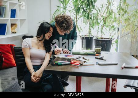 Two students collaborating on a creative project at a desk with markers and notebooks Stock Photo