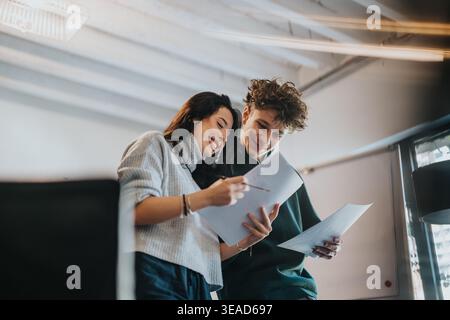 Two students reviewing papers together and smiling while collaborating in a modern study space Stock Photo