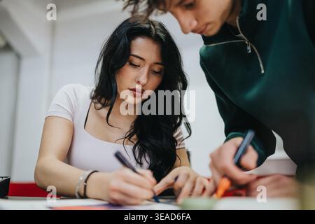 Two students studying together in a classroom collaborating on a written project Stock Photo
